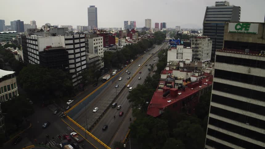 An aerial view pulls back over a busy sunken highway revealing the sprawling cityscape of Mexico City under an overcast sky