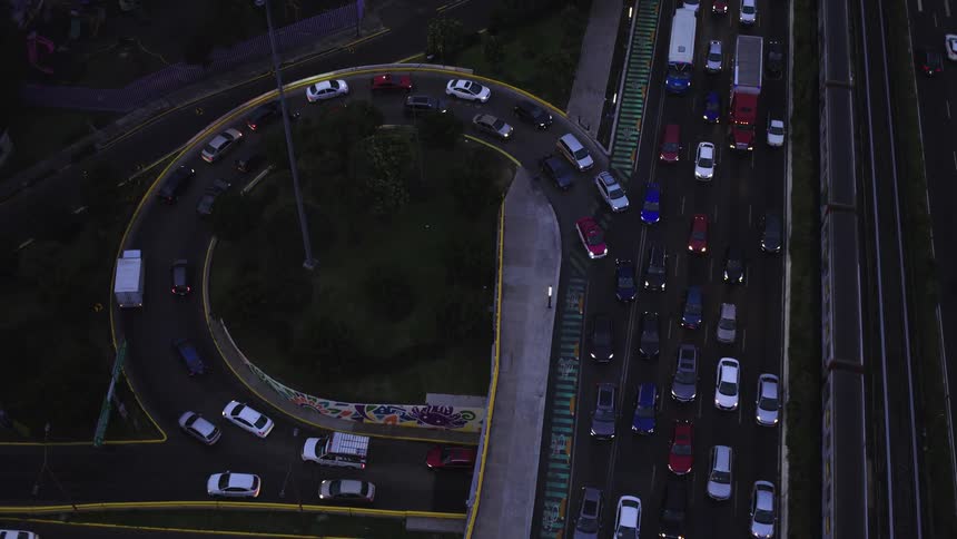 An aerial top-down view shows a massive traffic jam on a city highway and a curved interchange at dusk, as a train passes by