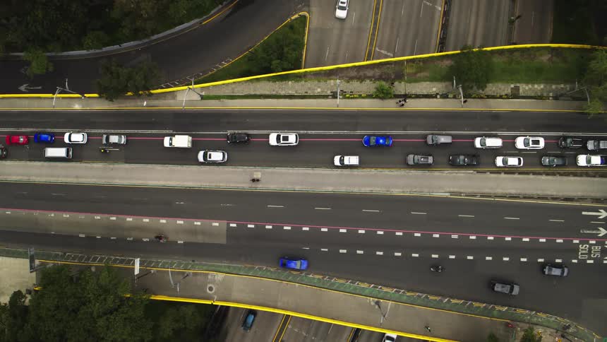 A top-down aerial view slowly zooms in on a busy city highway with congested traffic in some lanes and flowing cars in others
