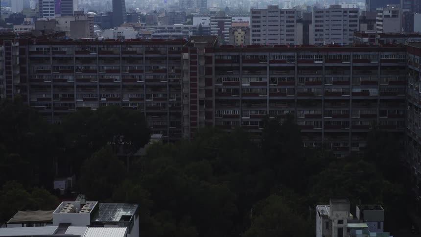 A slow aerial zoom reveals a large apartment complex surrounded by trees on a foggy, overcast day in a sprawling city
