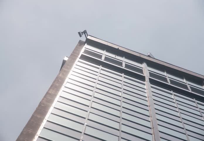 A slow zoom out from a surveillance camera perched on the corner of a modern, monolithic glass building under a grey sky