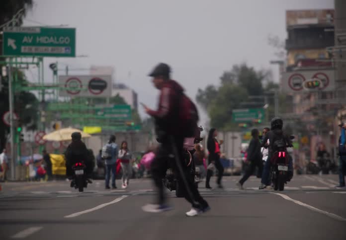 Slow-motion view of pedestrians crossing a busy street in Mexico City as motorcycles wait for the light to change