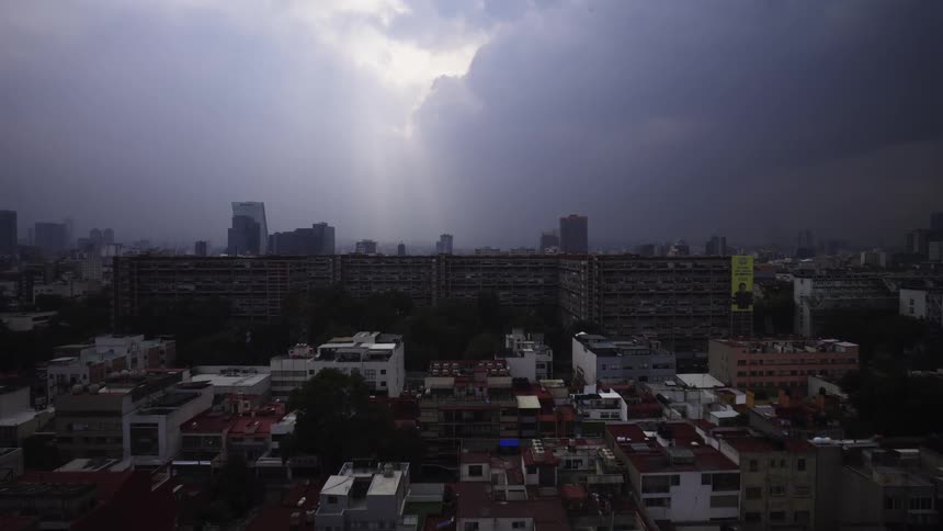 Aerial view of a sprawling city under dramatic storm clouds with rays of sunlight shining through