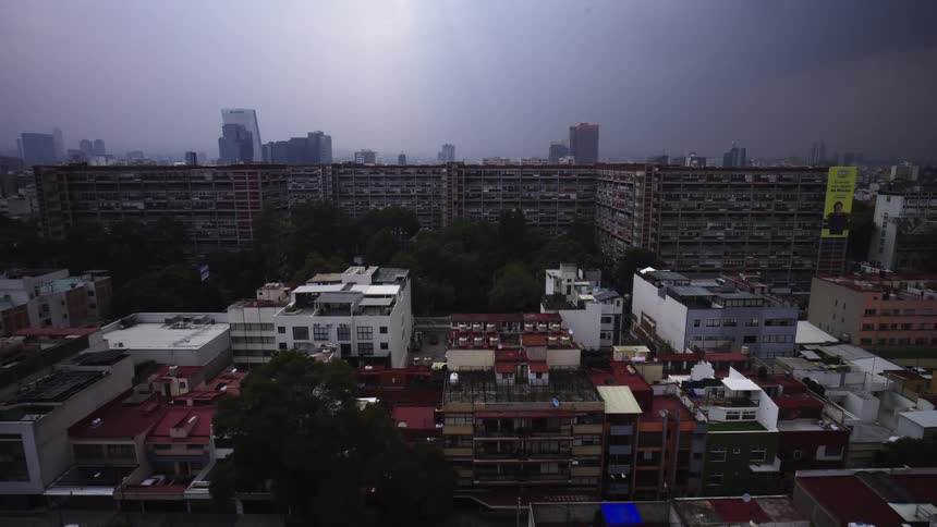 Slow aerial pullback reveals the diverse and densely packed buildings of a major city under a dramatic, cloudy sky