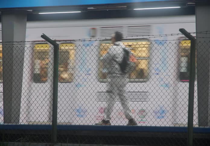 A tracking shot follows a colorful urban train covered in murals as it pulls into a station at night, with commuters waiting on the platform