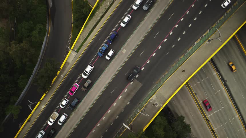 A top-down aerial view of a highway interchange shows heavy traffic in some lanes and free-flowing cars in others, with a slow zoom out
