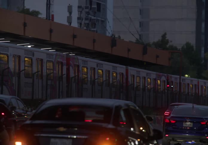 A Mexico City subway train travels on an elevated track above congested city traffic during a gloomy evening commute