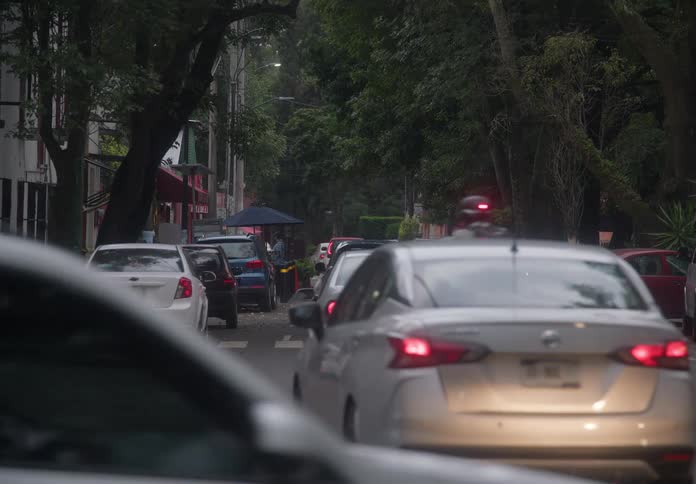 Slow-moving traffic congests a tree-lined city street on a gloomy, overcast day