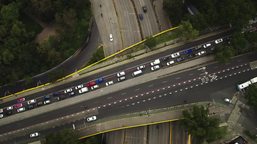 A static top-down aerial view of a busy highway overpass with congested traffic, while cars flow freely on the roads below