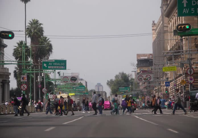 A ground-level view zooms out from pedestrians crossing a wide, busy street at an intersection in Mexico City