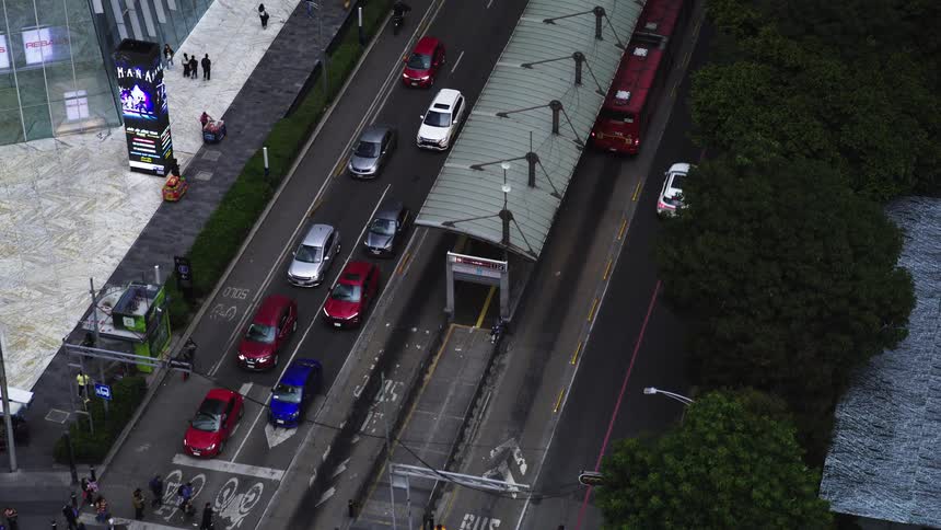High-angle aerial view pulls back to reveal bustling city traffic, a red public bus, and a crowd of pedestrians at a crosswalk