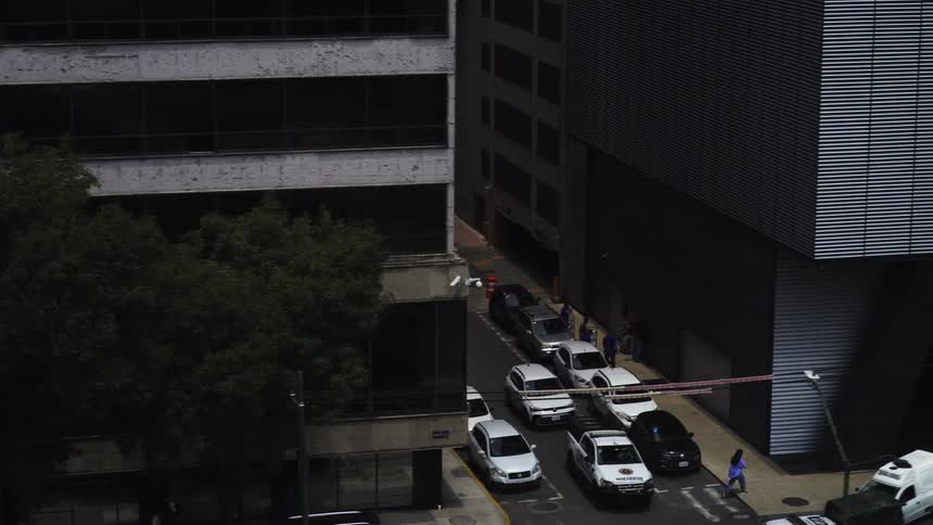 A slow zoom-out from an urban building reveals a street blocked off by a barrier and security vehicles