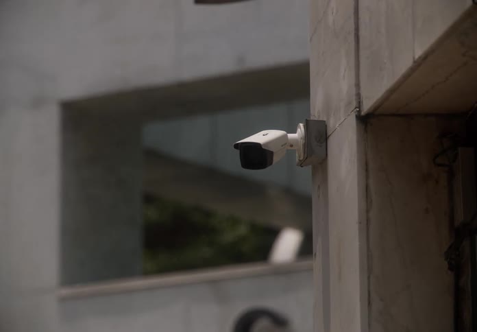 A slow zoom-in on a white security camera mounted on the exterior of a marble building