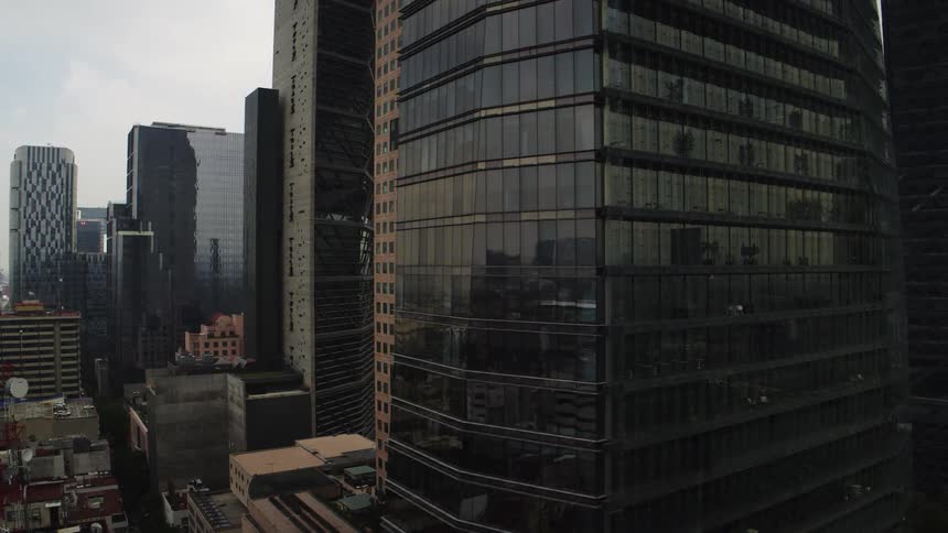 A slow aerial pan past a modern glass skyscraper reveals a dense urban financial district on an overcast day