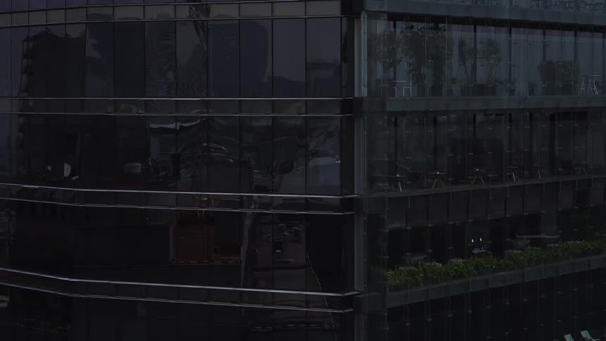 Moody aerial shot panning across the dark, reflective glass exterior of a contemporary high-rise office building