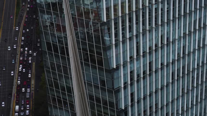 A close up aerial shot zooms out from a modern glass skyscraper to reveal the busy city traffic below
