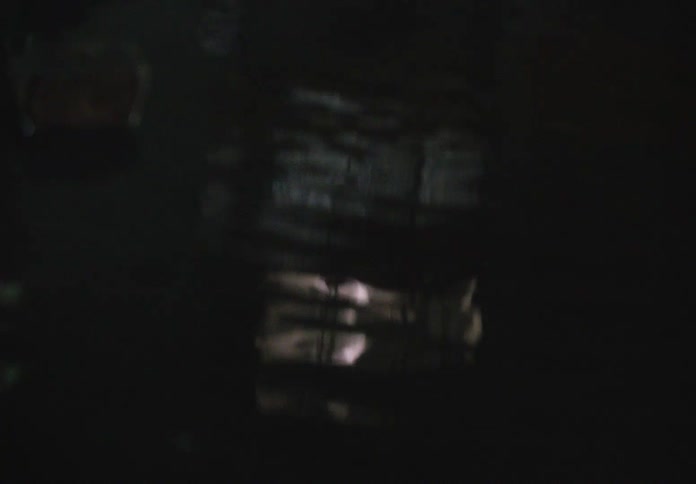 A distorted reflection shows a person's silhouette moving inside a lit apartment window at night before the view dissolves into dark, blurry ripples
