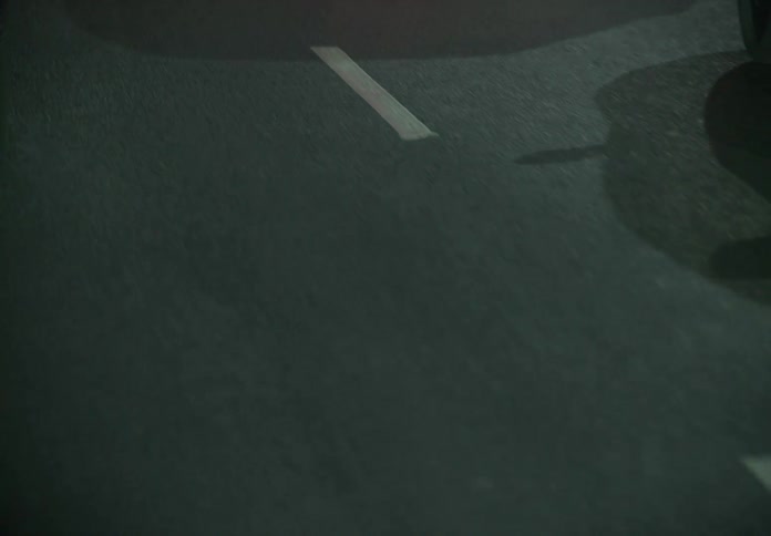 A low-angle close-up shot of the road as a car drives along the highway at night, with lane markings passing by