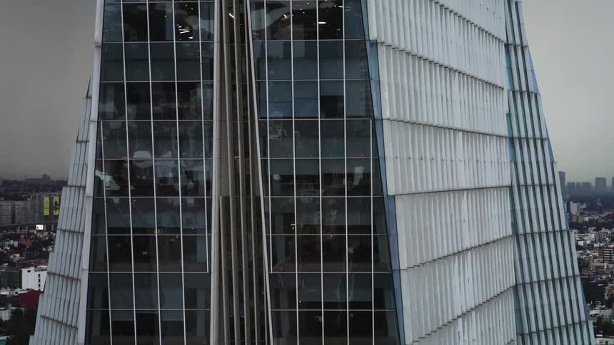 An aerial drone shot slowly ascends the modern glass facade of the MetLife skyscraper, revealing the sprawling city below under a cloudy sky