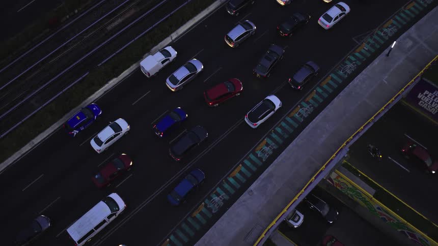An aerial top-down view of a highway interchange shows heavy traffic at night, slowly revealing the sprawling city transportation network