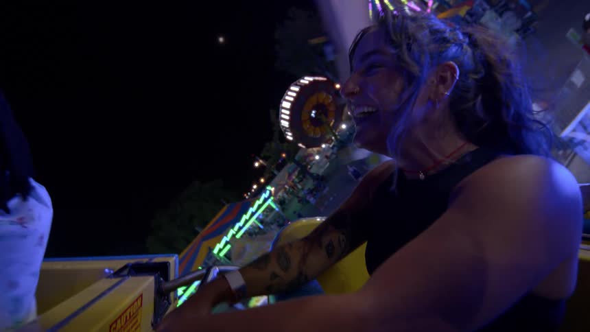 A joyful woman with tattoos laughs and screams in slow motion while on an exhilarating spinning ride at a carnival at night