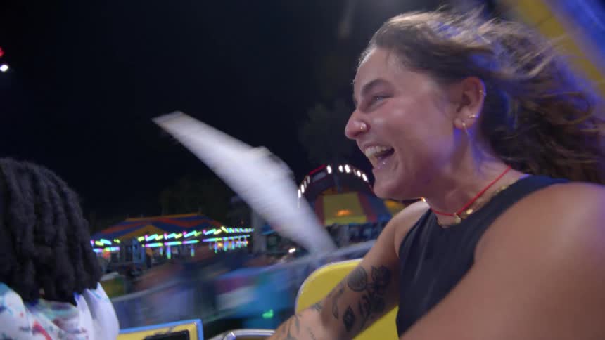 A joyful woman laughs and screams with excitement while riding a fast-spinning carnival ride at night in slow motion