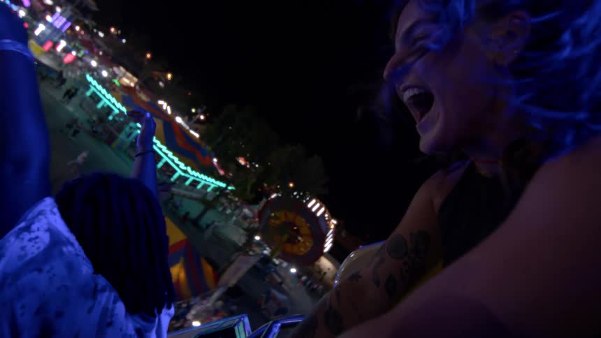 A slow-motion point of view shot of two friends laughing and screaming on a thrilling carnival ride at night