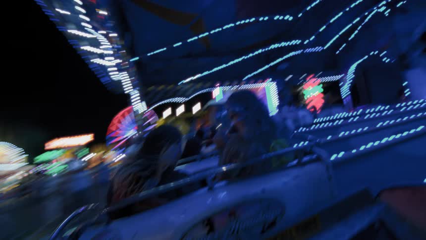 Point-of-view shot of two friends enjoying a fast-spinning ride at a vibrant, brightly lit carnival at night