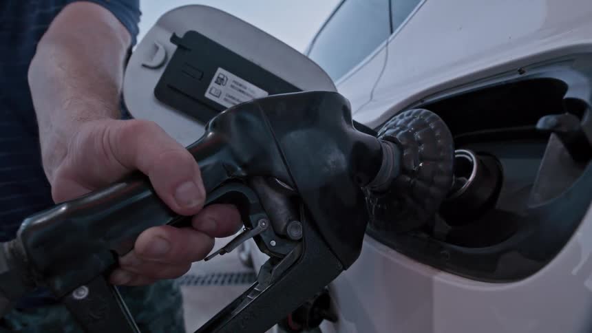 A close-up of a hand squeezing a gas pump handle to refuel a white car at a gas station