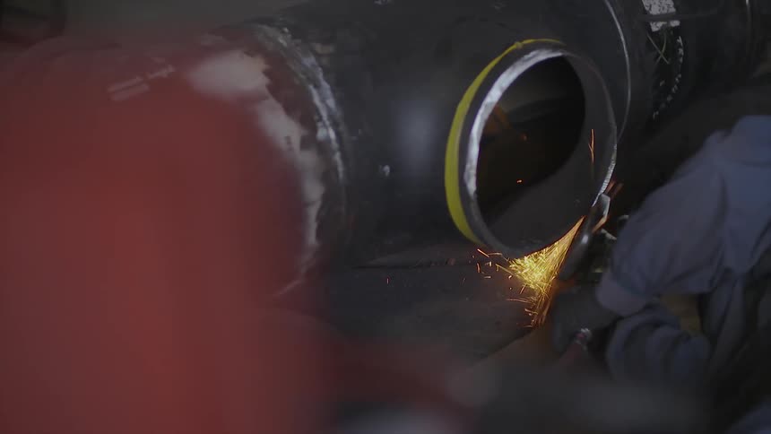 A worker is sawing the side of a pipe