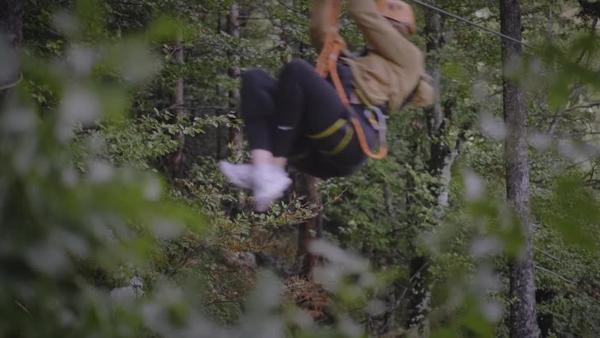 A woman in a harness and helmet enjoys a fast zipline ride through a lush green forest