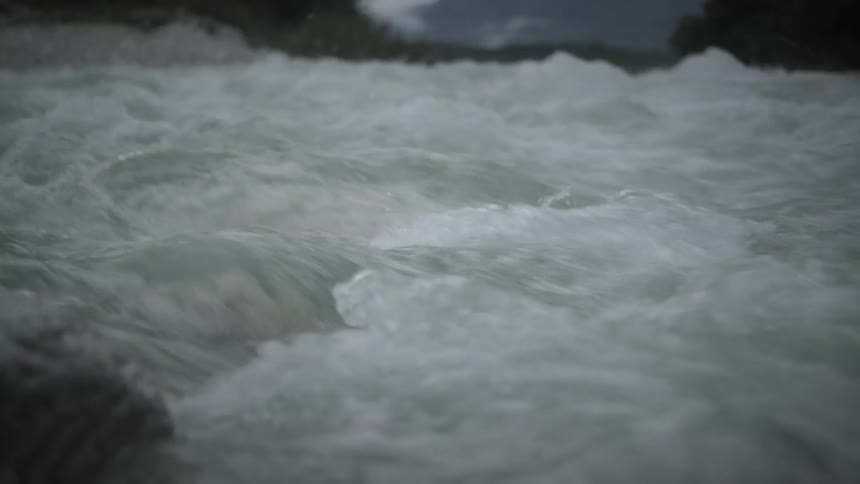 A close-up, slow-motion view of powerful river rapids churning on a gloomy, overcast day