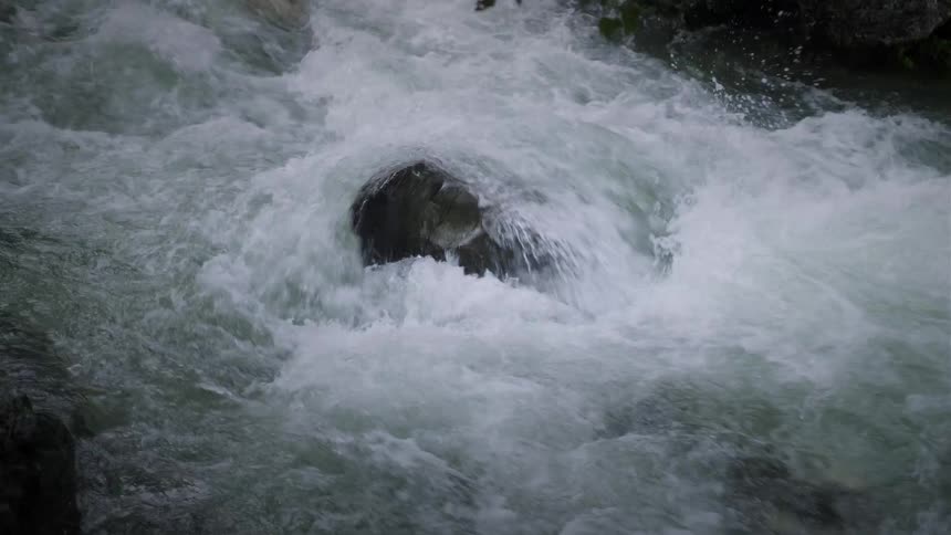 A close-up shot of a turbulent river with white water rapids flowing quickly around a large boulder