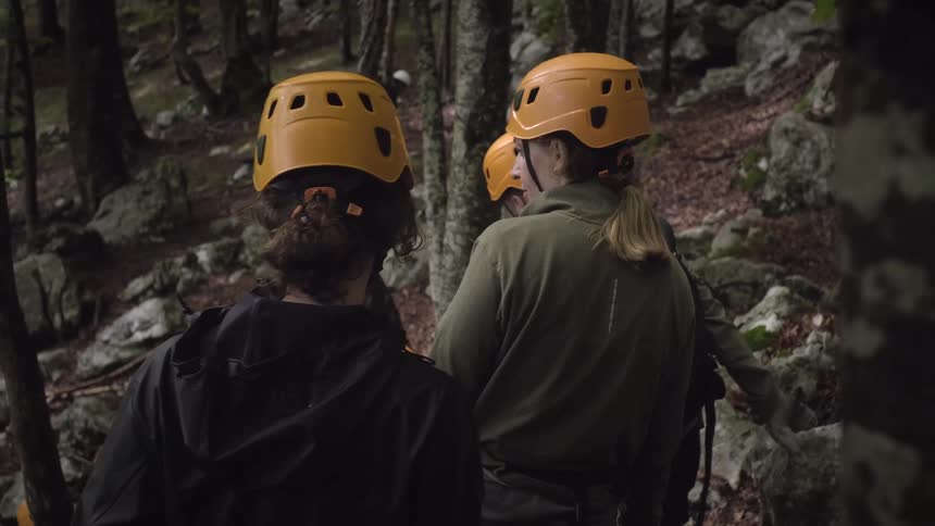 A group of friends equipped with helmets and gear hike through a rugged forest on an outdoor adventure