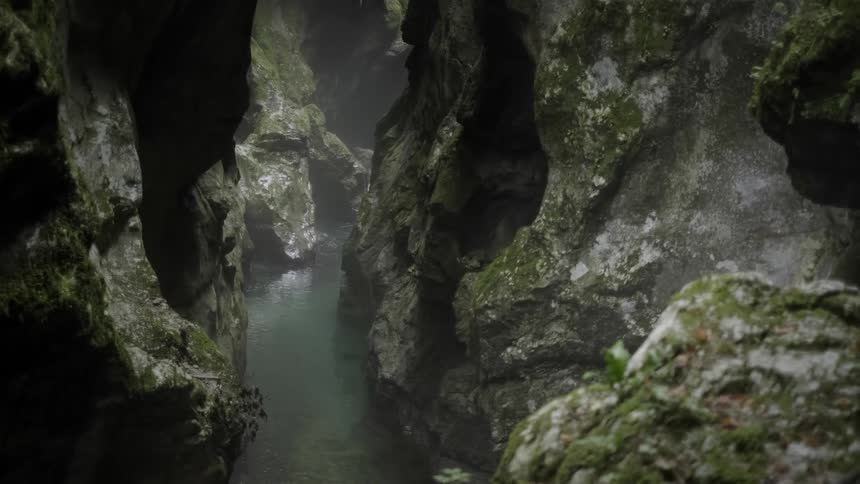 A clear river flows through a misty and mossy canyon deep within a mysterious cave
