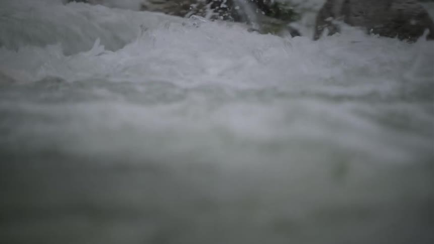 An immersive, water-level view shows a turbulent river surging through a rocky bed in slow motion