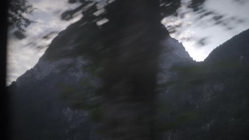 A majestic mountain range is revealed through the swaying leaves of trees in the foreground