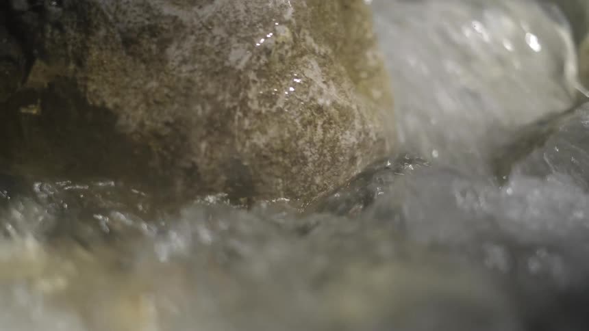 A powerful stream of water cascades over weathered rocks in a mesmerizing close-up, slow-motion shot