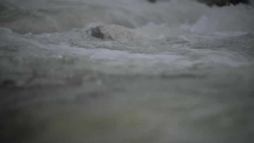 An immersive slow-motion, close-up shot of a turbulent river rushing over a rocky riverbed