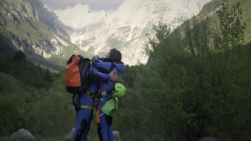 Two male friends in wetsuits happily hug and embrace in a beautiful mountain valley after a canyoning adventure
