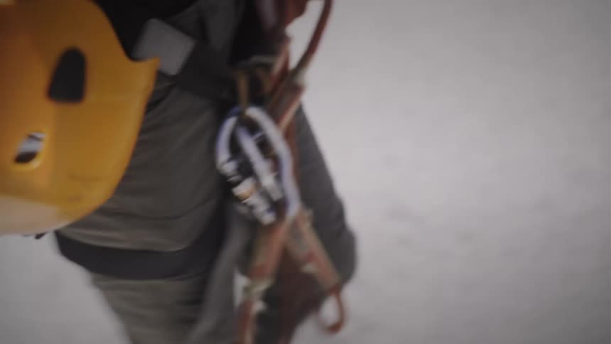 Slow-motion close-up of a mountaineer's harness and climbing gear as they trek through a snowy landscape