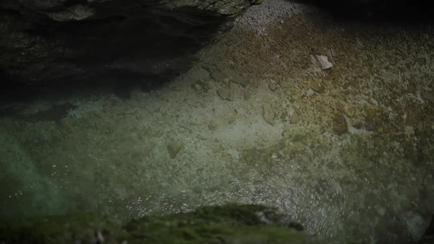 Top-down view of crystal-clear water flowing gently over a pebble riverbed inside a dark, rocky cave