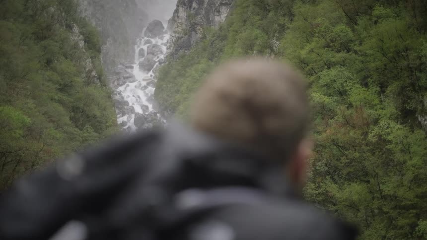 A couple of hikers look out over a stunning waterfall cascading down a lush, green mountain valley