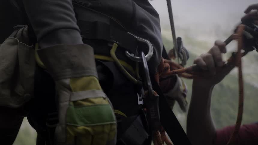 Close-up of a rock climber's partner adjusting their safety harness and ropes before a climb