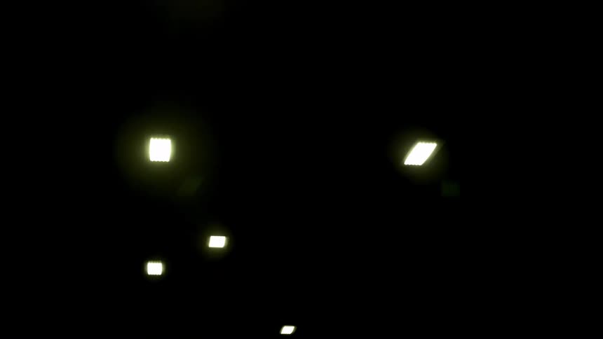 A vehicle's point-of-view looking up at ceiling lights while driving through a dark underground tunnel