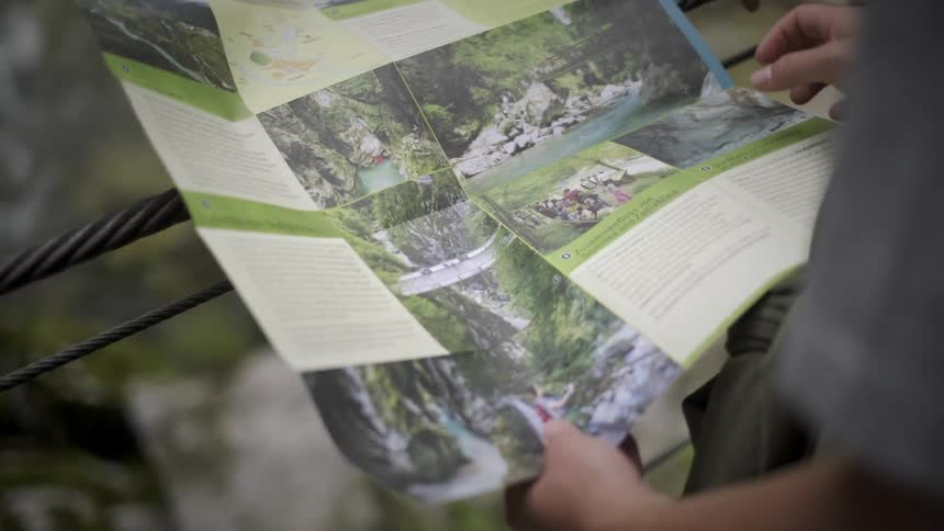 Close-up over-the-shoulder shot of a person pointing at a location on a trail map with a rushing river in the background