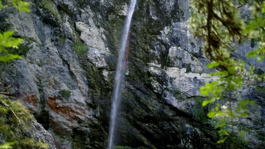 An adventurous person canyoneering down a tall, scenic waterfall in a rocky gorge