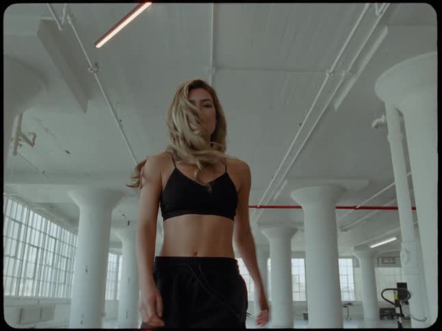 An athletic woman with long blonde hair confidently turns towards the camera in slow motion in a spacious industrial loft