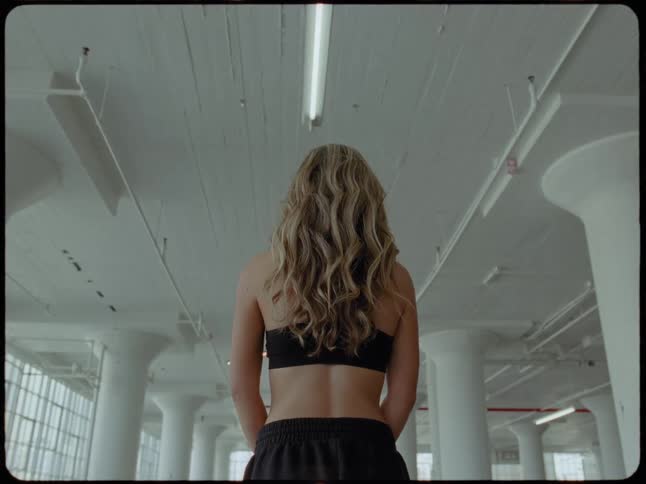 Low angle shot from behind a woman with long blonde hair standing in a large industrial loft space