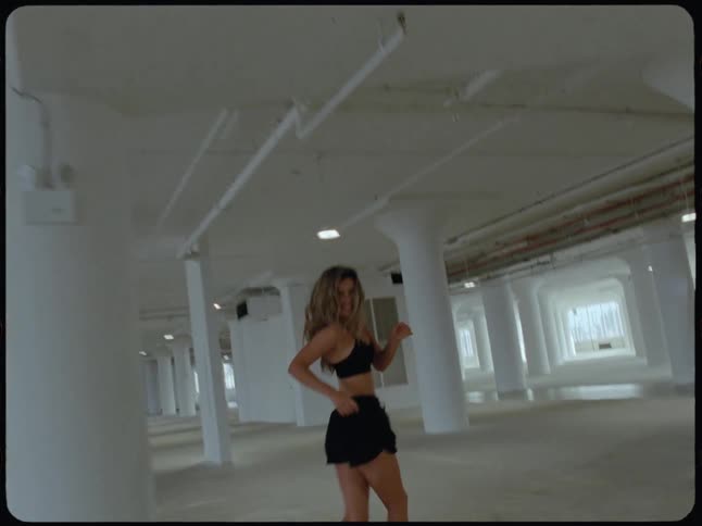 A woman in activewear runs energetically through a large empty industrial building in slow motion